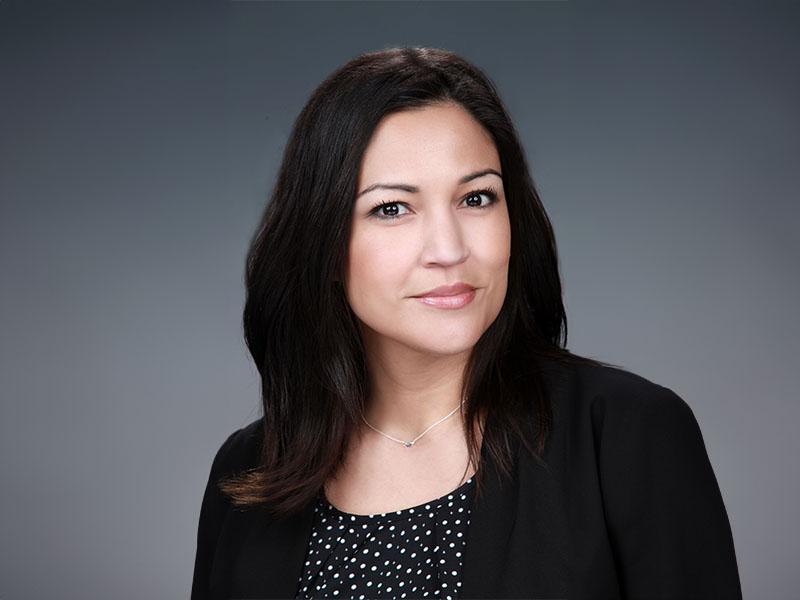 headshot of Nicole Castilleja-Bentley, pictured looking toward the camera in a black blazer against a great background